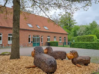 Das Bild zeigt das Gebäude der Krippe Sonnenblume mit den 3 Schafstatuen aus Holz im Vordergrund und dem Eingang zur Krippe im Hintergrund
