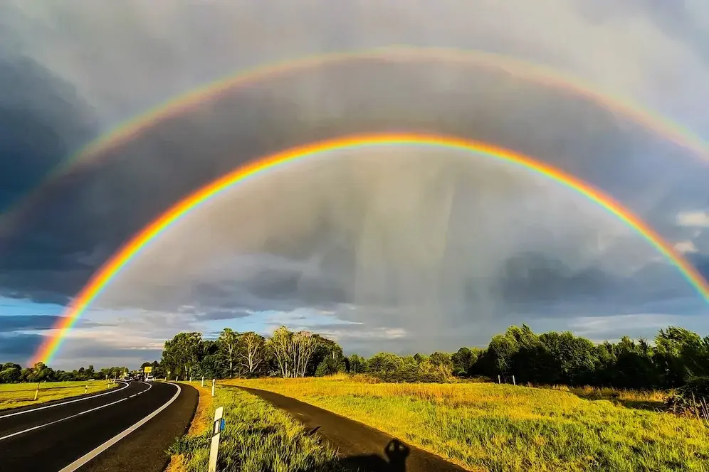 Ein doppelter Regenbogen über einer Landstraße und Natur.