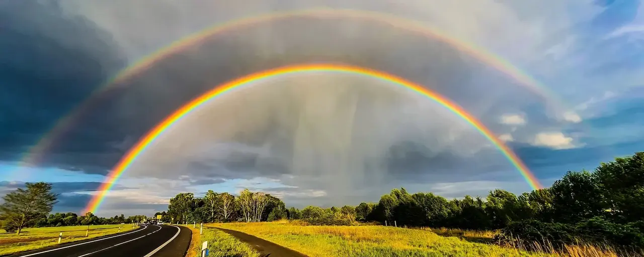 Ein doppelter Regenbogen über einer Landstraße und Natur.