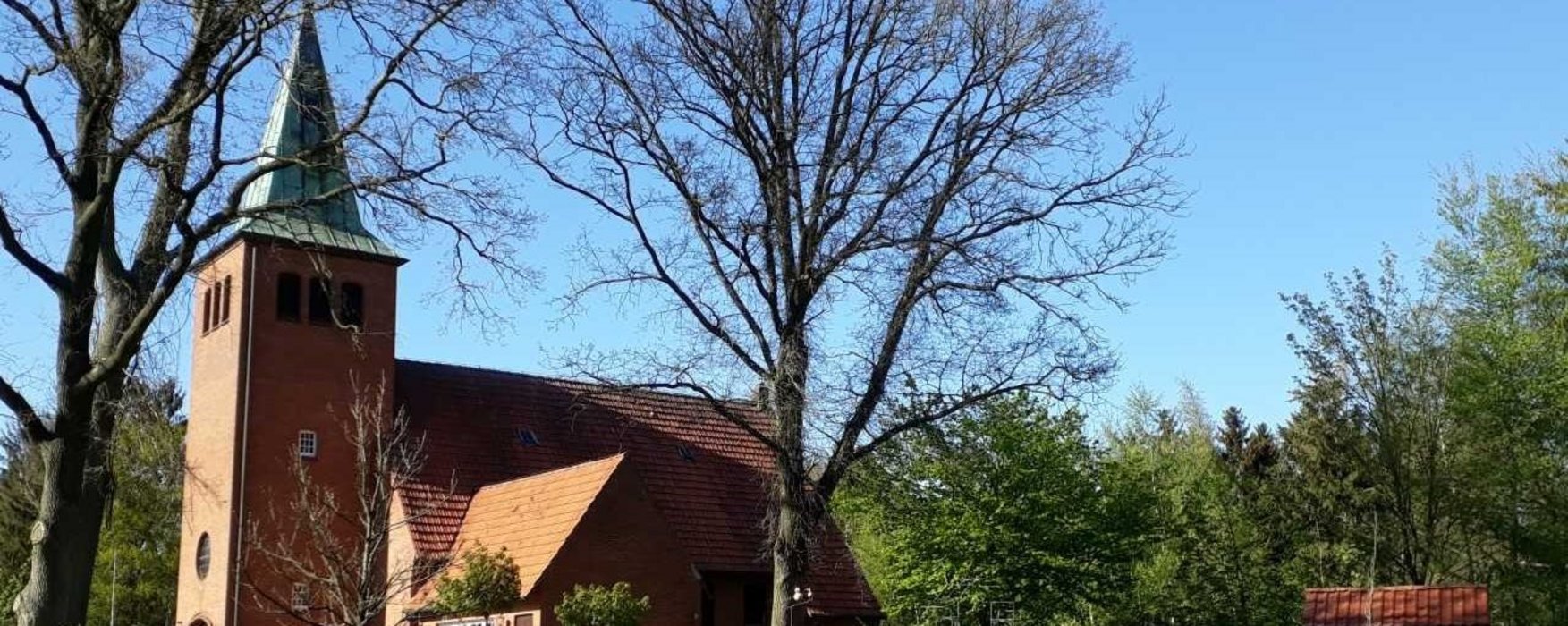 Es ist die Kirche Benthullen zu sehen, die Sonne scheint, die Bäume sind noch nicht vollständig belaubt