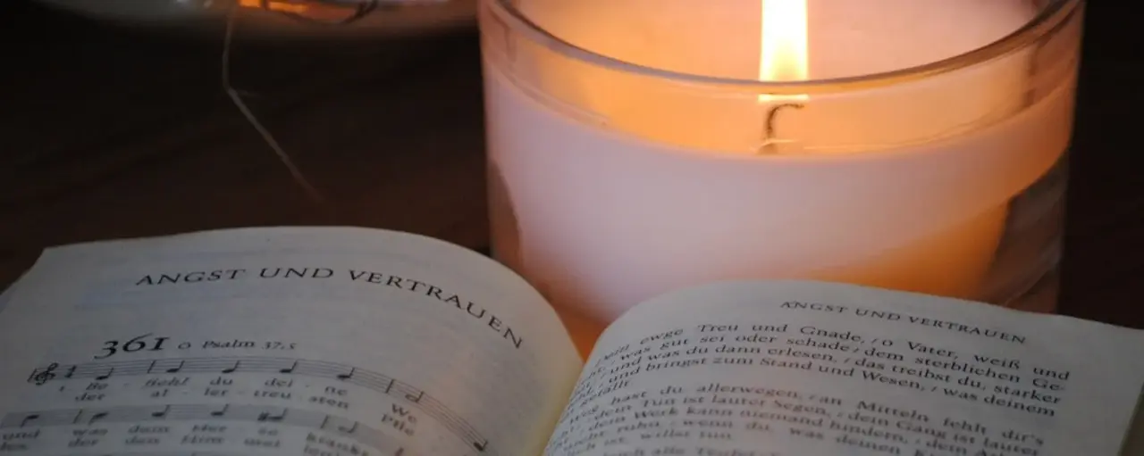 Aufgeschlagenes Evangelisches Gesangbuch mit Nummer 361; dahinter brennt eine weiße Kerze.