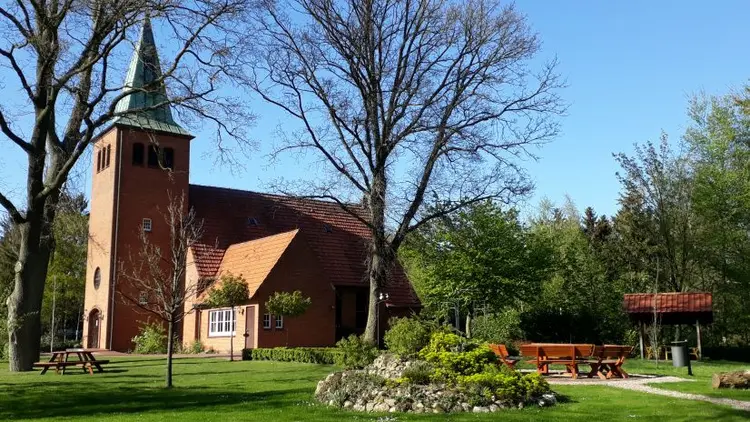 Die Benthullener Kirche wird gezeigt, vom Garten aus gesehen. Die Sonne scheint auf die Kirchenmauern, die Bäume sind kahl.